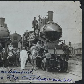 Unknown gentlemen in hats in front of locomotives, among railway workers
