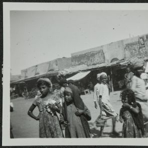 Little girls and other passers-by in front of the row of shops