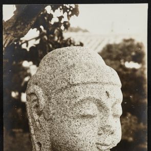 Black and white photo of Buddha head placed on stone pillar