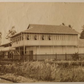 Two-story building with a covered terrace and tropical vegetation