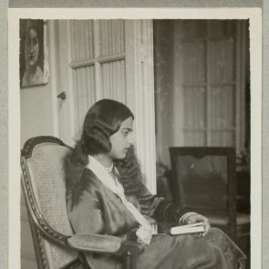 Amrita sitting in an armchair in their Paris home, with a book in her hand