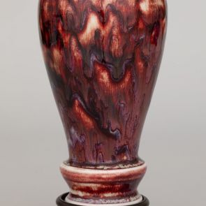 Vase with flowy red glaze, on a carved wooden stand