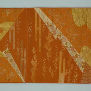 Japanese obi design sample with golden and silver susuki grass in front of a dark pinkish orange background