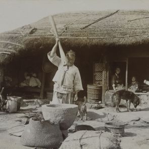 Korean peasant husking rice outside his house
